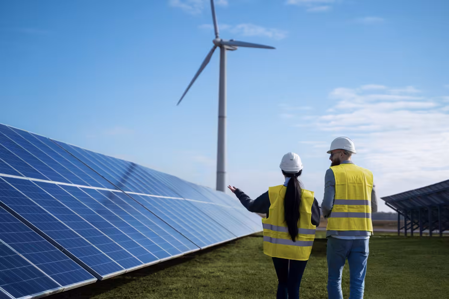 Two people standing in front of solar panels and wind turbines.